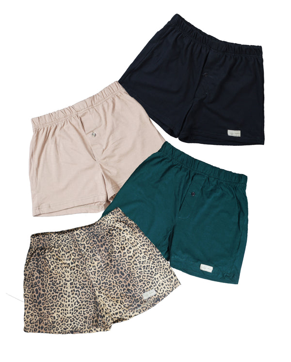 Front view of four pairs of Go Wild Boxers, one Black, one Tan, one Green, and one Leopard Print. Each have an elastic waistband, a buttoned front fly, and a Tag Buffalo label on the bottom front of the left leg. 100% cotton.