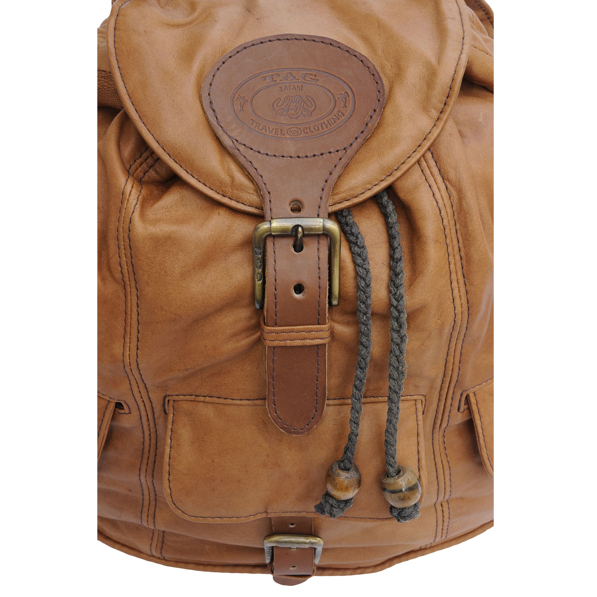 Close-up of a Tag Safari Impala Leather Backpack in Tan. Shows a top flap with buckle and embossed Tag logo, top-closure draw cords, and a flap-covered front pocket with buckle.--3